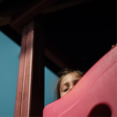 a young girl peeking her head out behind a red slide